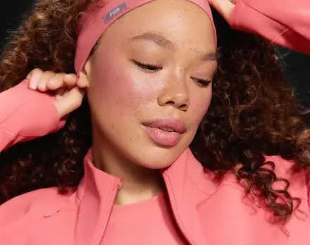 Close-up portrait of a model wearing the Pulmonary Pink scrub collection with a matching headband and zip-up jacket, highlighting the soft pink colorway and coordinated styling.