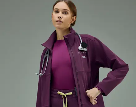 Healthcare professional wearing Deep Purple and Celery FIGS FlexKnit scrubs with matching drawstring pants and athletic sneakers.