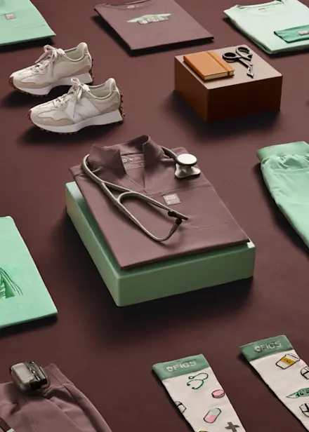 Folded FIGS x Star Wars scrub sets in Smokey Taupe and Jade displayed with a stethoscope, showcasing the limited-edition collection.