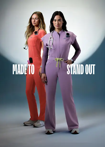 Two healthcare professionals wearing FIGS scrubs in Purple Haze and Fireside from the latest color collection with the message "Made to Stand Out."