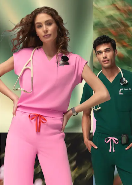 Female healthcare professional in Sunrise Pink scrubs and male healthcare professional in Forest Green scrubs standing side by side to introduce the FIGS Spring Drop collection.