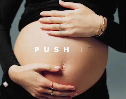 Close-up of a pregnant belly with hands gently resting on it, highlighting the "Push It" campaign for the FIGS Maternity Collection.