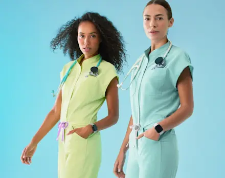 Healthcare professionals model the Sea Mist and Seaglass limited-edition FIGS scrubs against a blue studio backdrop.