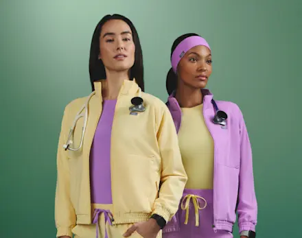 Two healthcare professionals wearing FIGS bomber jackets and scrubs in Butter Yellow and Wild Iris from the Never Change collection.